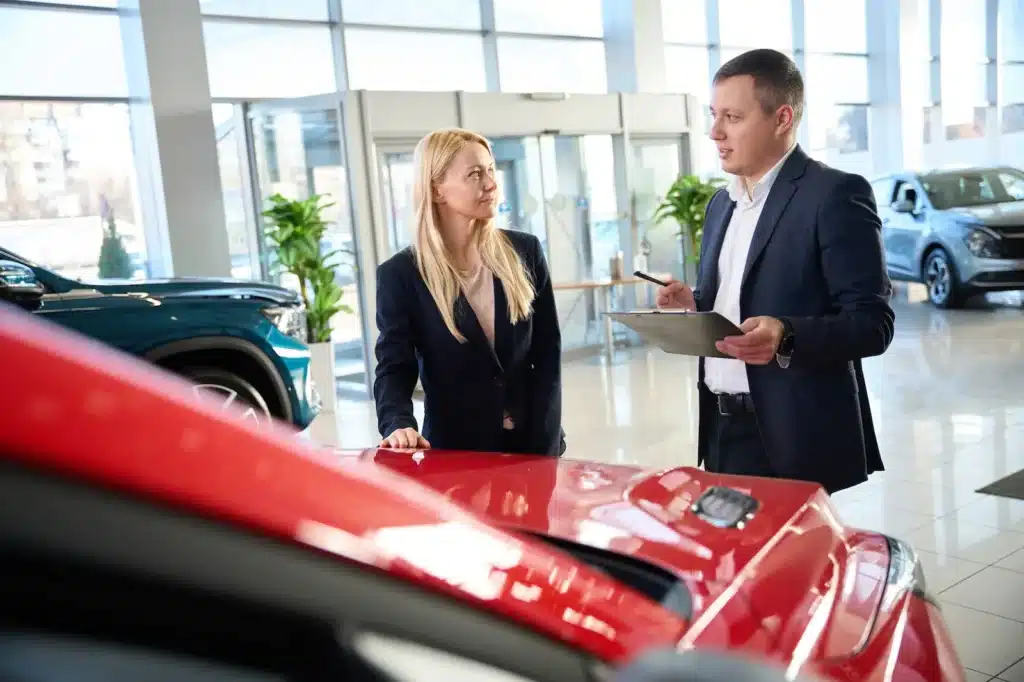 Two people talking beside a car in a sales showroom