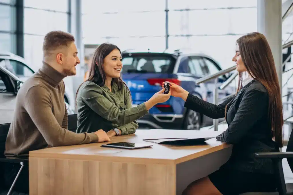 A salesperson handing car keys to a young couple