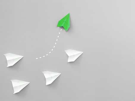 Green paper plane leads white planes creatively.