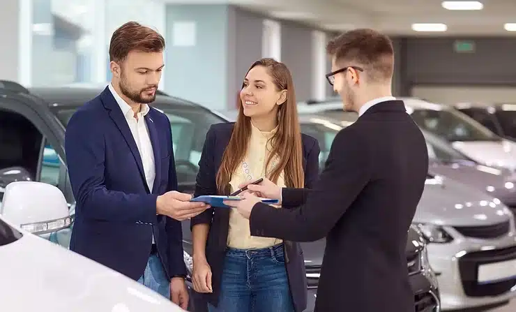 Customers signing documents at car dealership.