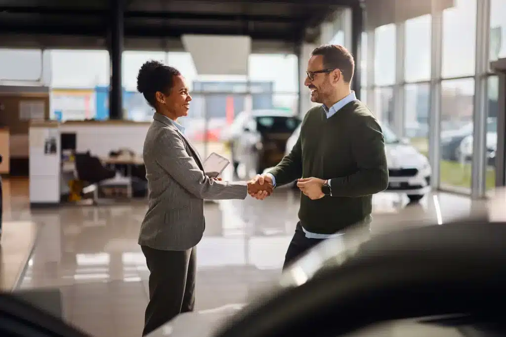 Two people shaking hands in a car dealership.