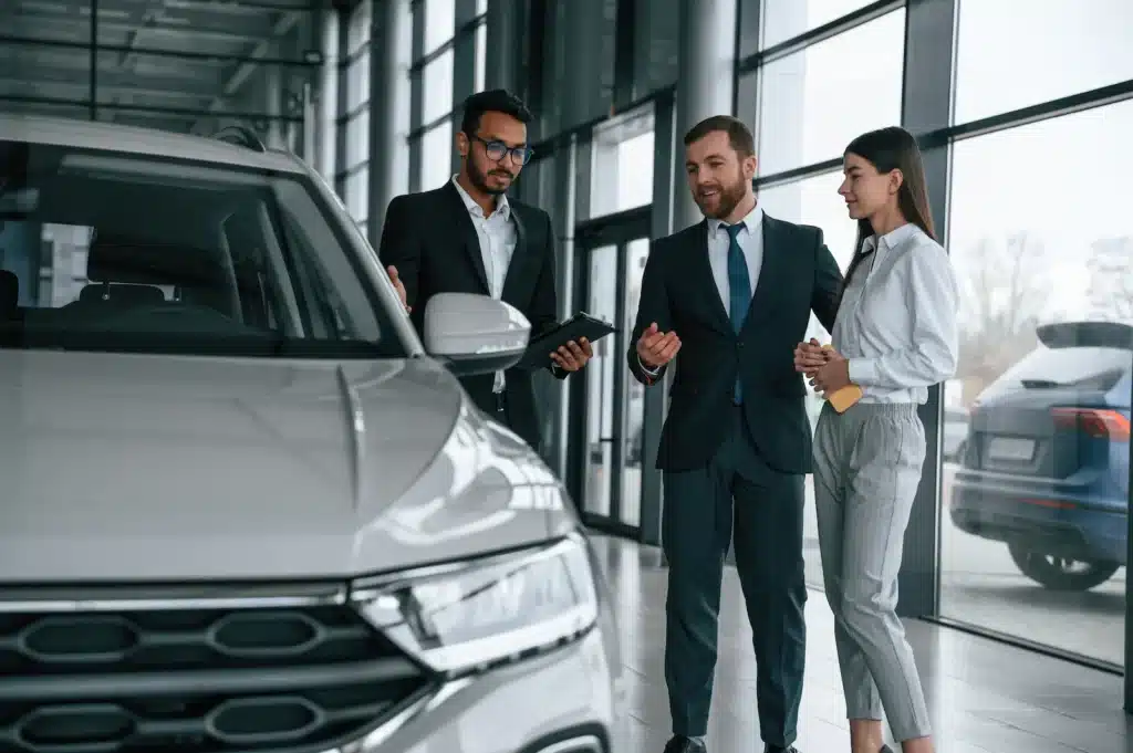 Car dealer showing vehicle to couple in showroom.