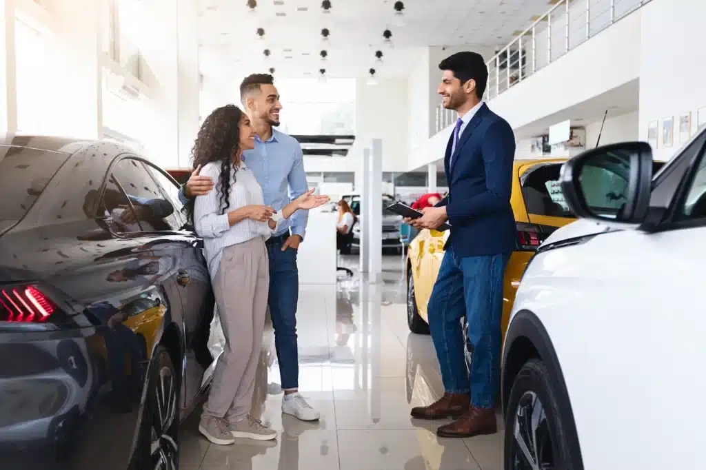 Couple consulting salesman in car dealership showroom.